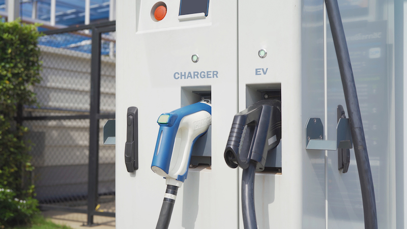 Hand pulling in cable from EV car charger or electric vehicle station. Cable connected at gas station, power supply battery charging an alternative eco environment future technology energy innovation